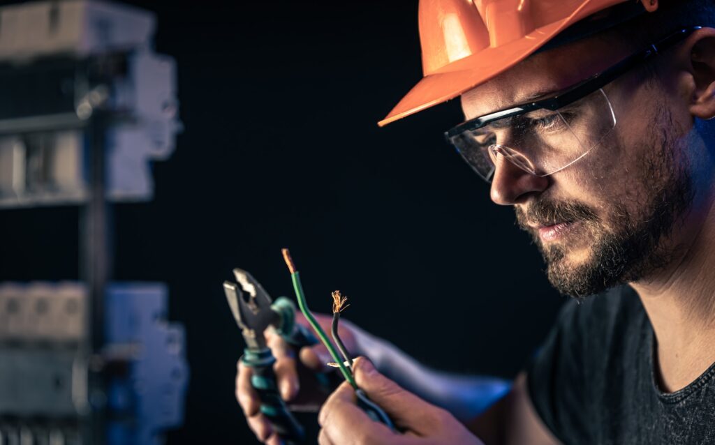 A male electrician works in a switchboard with an electrical connecting cable.